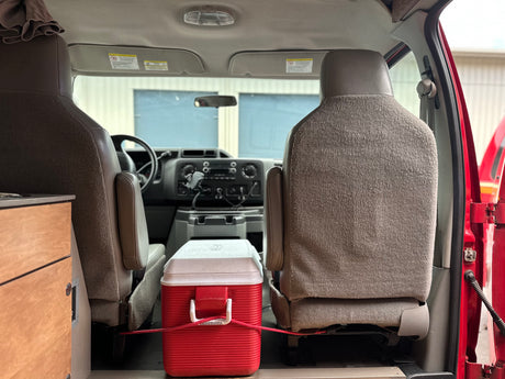 RV rental interior: Front seats, dashboard, and a cooler secured for travel. Ready for a new adventure.