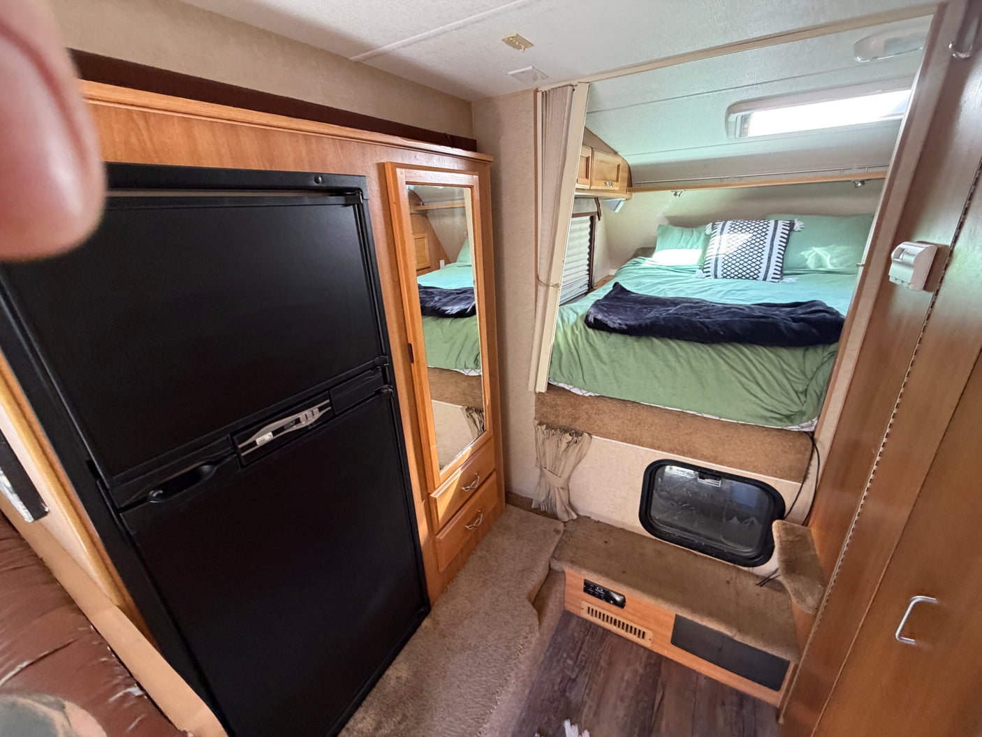 Cozy rv rental interior: A compact camper with a comfortable bed, black refrigerator, mirrored storage, and wood accents.