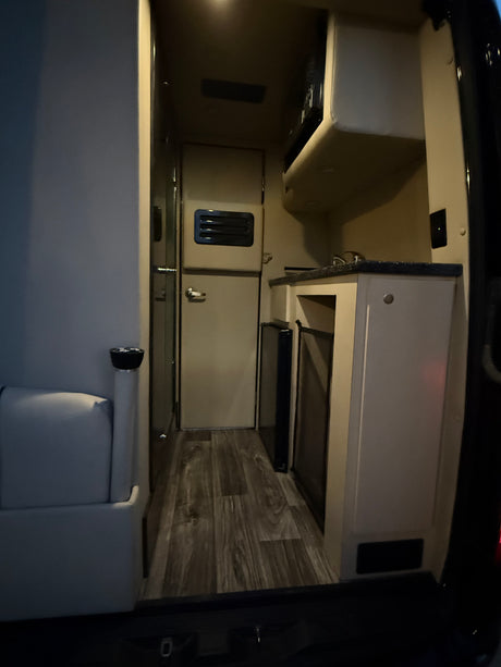 Step inside this RV rental, showcasing a compact kitchen, comfy seating area, and wood-look flooring.