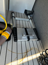 Interior RV rental storage: collapsed ladder, sewage/water hoses, and stains on faux-teak flooring.