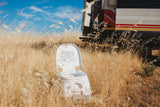 Experience RV rental freedom! Portable toilet amidst golden dry grass, with a camper van parked behind for off-grid comfort.