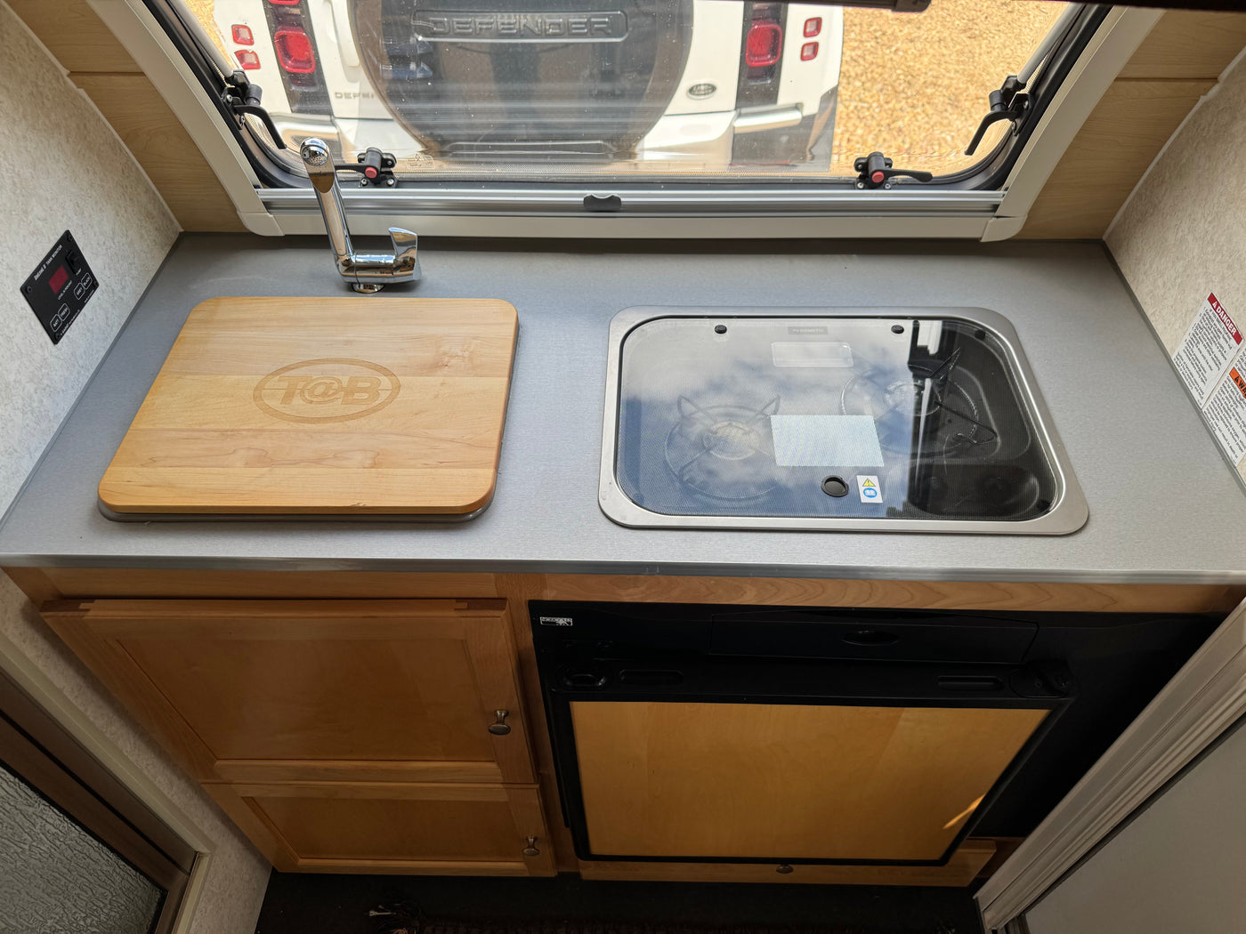Inside an RV rental: a compact kitchenette with sink, covered stovetop, cutting board, and refrigerator, perfect for travel. — photo 15