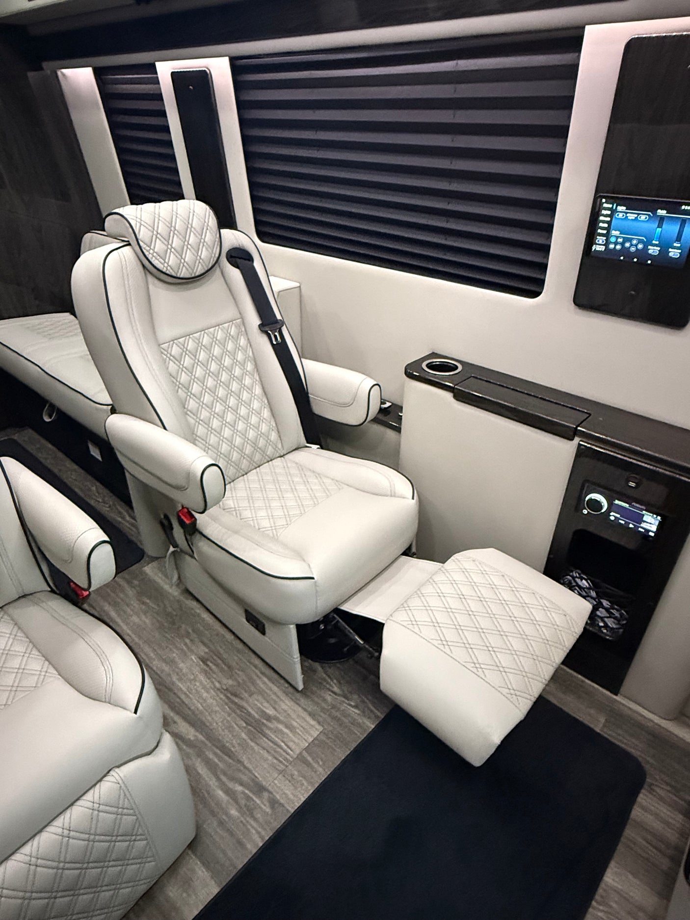 Interior of a luxury RV rental van: White quilted leather seats, extended footrests, and modern controls for premium comfort.