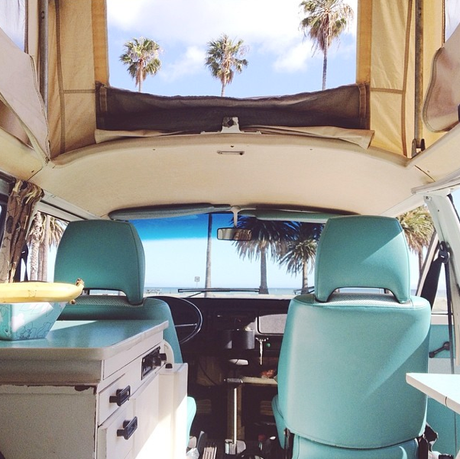 Relaxing inside a classic RV rental. Teal seats, a pop-top roof, and stunning palm tree beach views from this retro camper van.