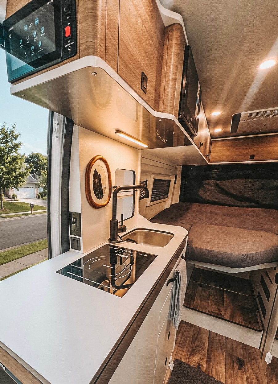 Modern RV rental interior: compact kitchen with induction cooktop, sink, and comfy bed for travel adventures.