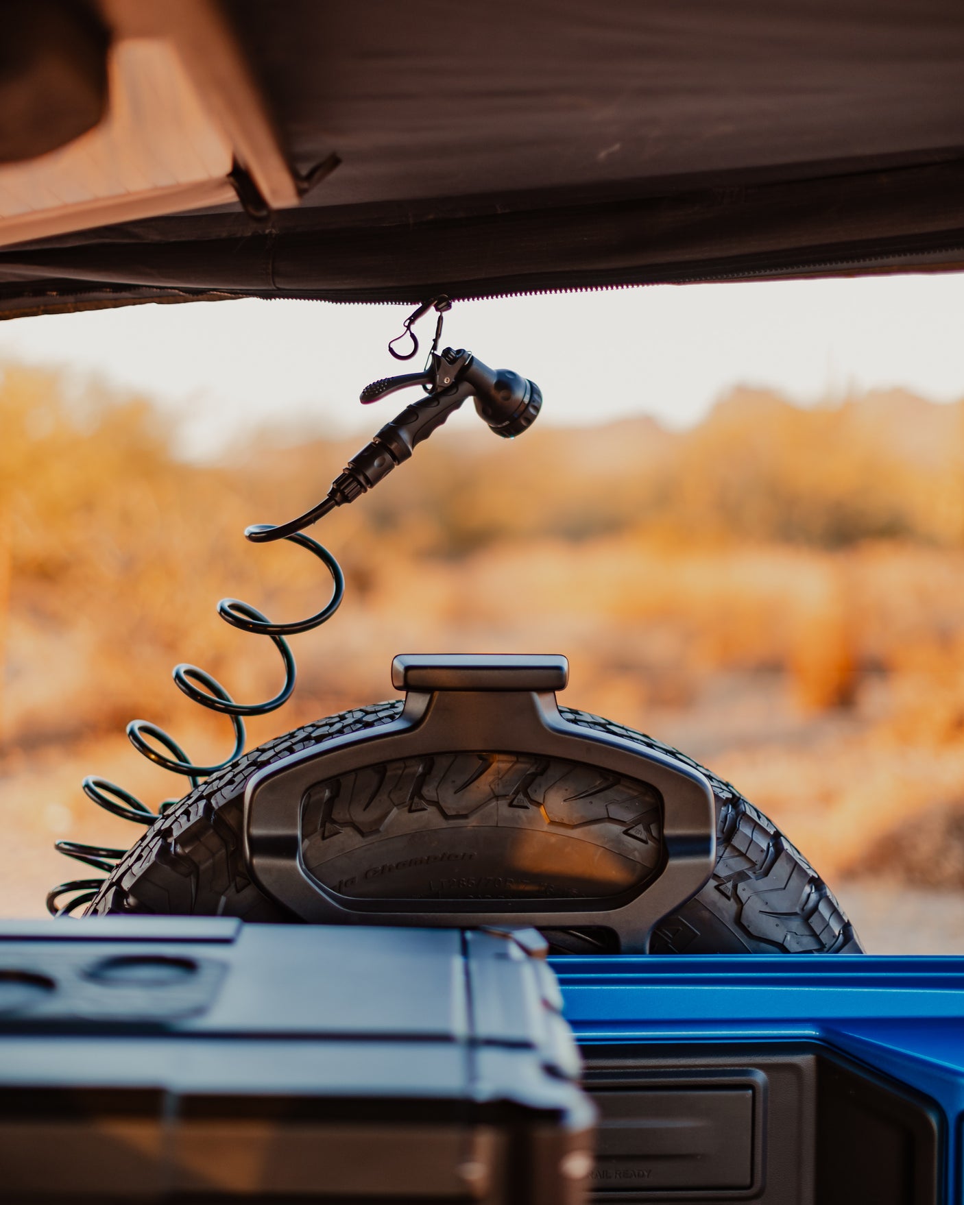 RV rental adventure awaits! Portable shower hangs near an off-road vehicle's spare tire, ready for outdoor cleaning.