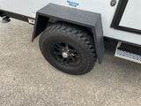 Side view of a Braxton Creek rv rental unit, showcasing its rugged tire, black fender, and stabilizing features on gravel.