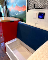 RV rental interior: open storage bench, red cabinet, mountain mural, and illuminated control panel with switches.