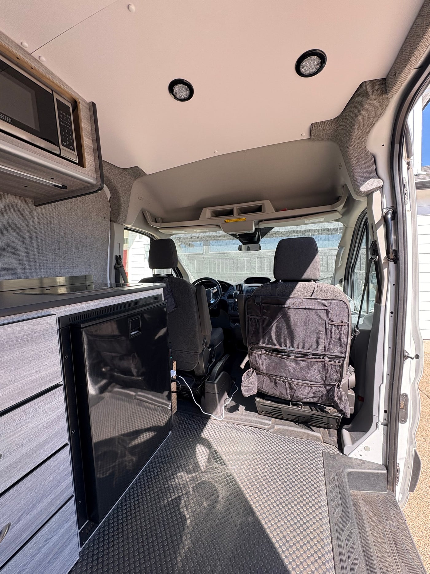 Inside this modern rv rental: a compact kitchen with microwave, fridge, and front cabin view. — photo 5