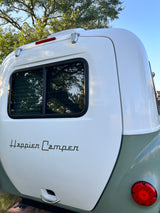 Detailed rear view of a white Happier Camper RV rental, showing its window, red taillight, and green lower body.