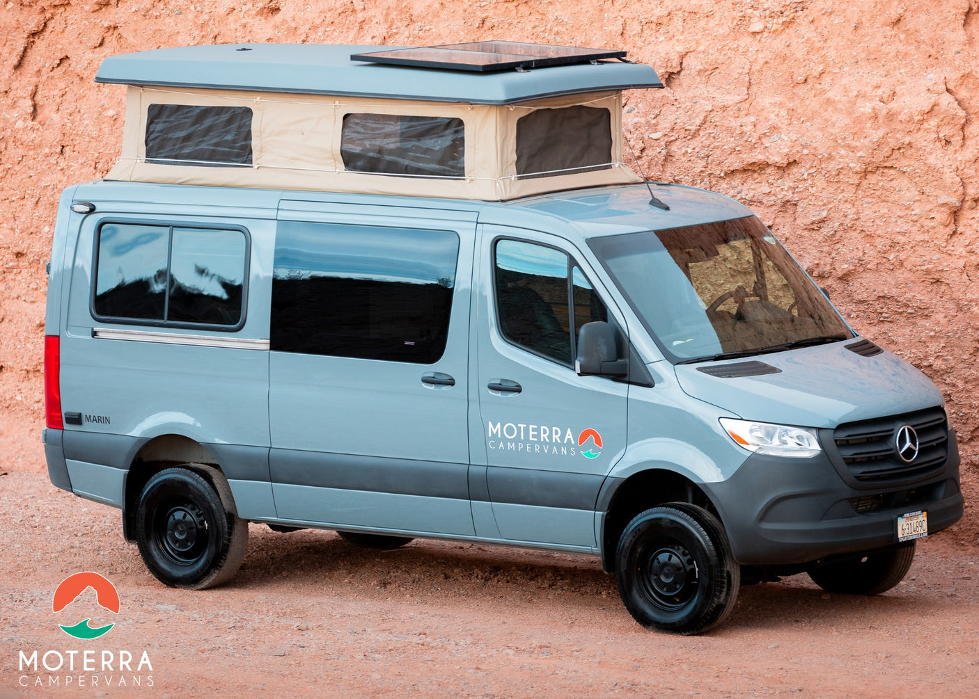 Grey pop-top camper van rv rental by Moterra parked in red rock terrain. Your next outdoor adventure awaits.
