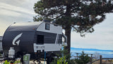 An RV rental (Go Lite travel trailer) at a scenic campsite overlooking misty mountains and a valley, near a large pine tree.
