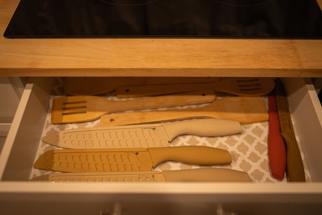 Open RV rental kitchen drawer neatly holds knives with sheaths and wooden cooking spatulas on a patterned liner.