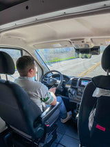 From passenger seat, a person drives an RV rental van. Interior shows dashboard, steering wheel, and front seats.