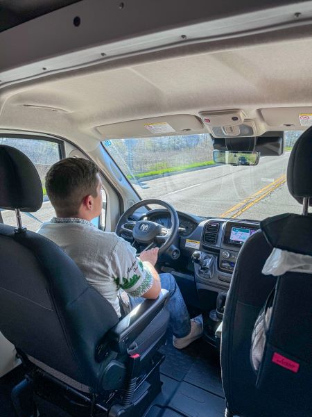 From passenger seat, a person drives an RV rental van. Interior shows dashboard, steering wheel, and front seats.