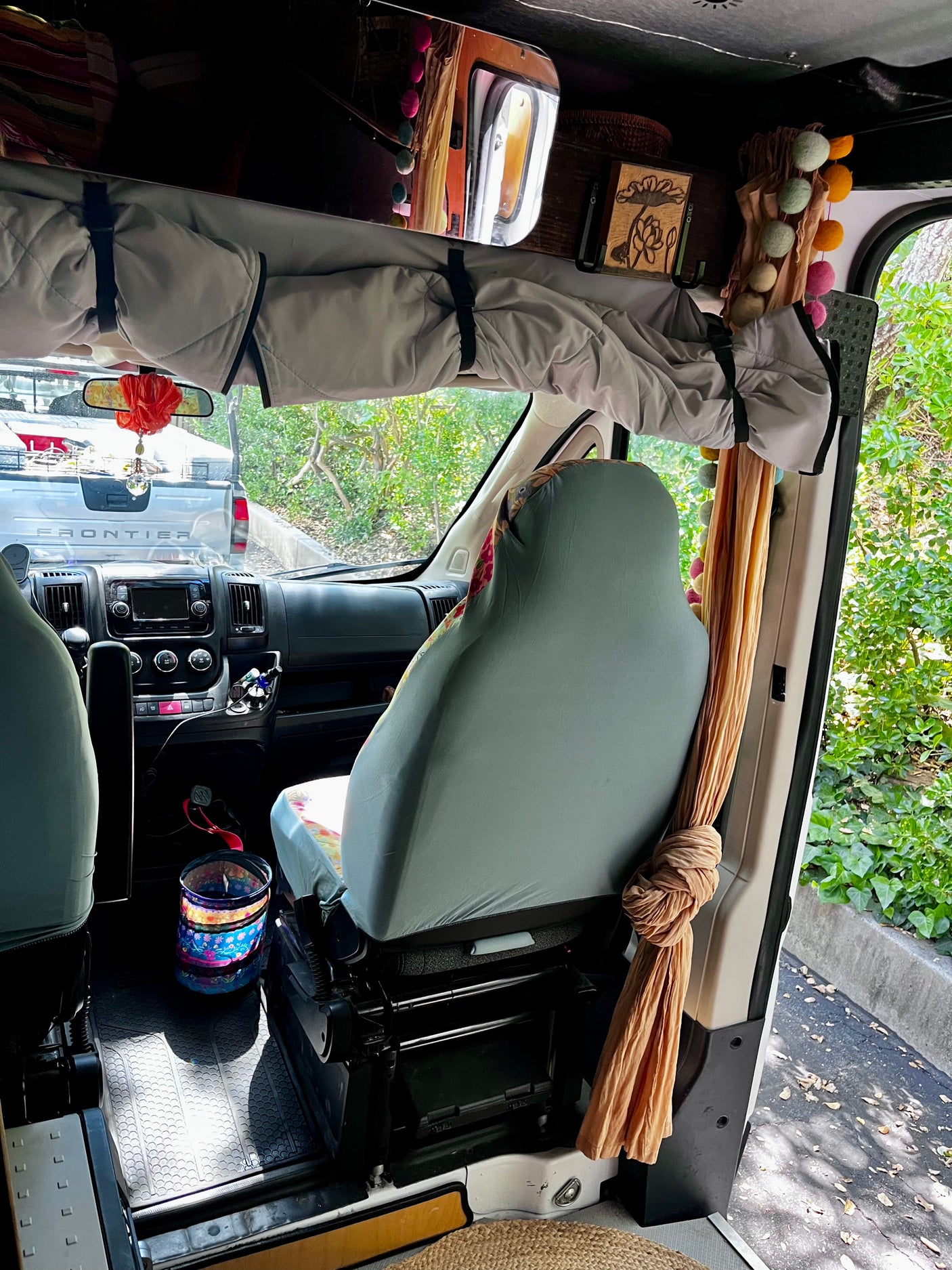 Discover this RV rental's front interior: comfy driver's seat, dashboard, and overhead storage with vibrant, colorful decor. Truck seen outside.