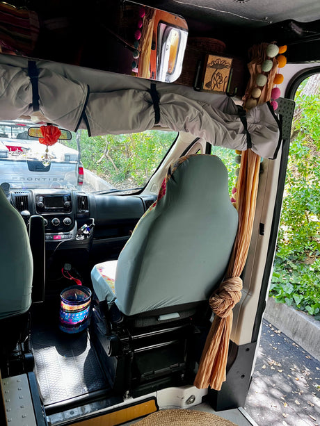 Discover this RV rental's front interior: comfy driver's seat, dashboard, and overhead storage with vibrant, colorful decor. Truck seen outside.
