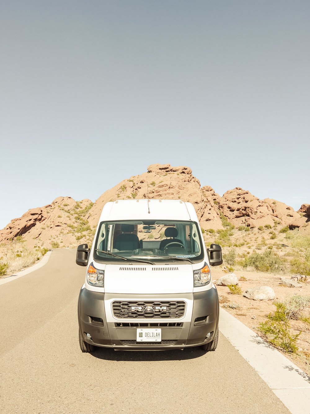 White RV rental van parked on a desert road amidst red rock formations under a clear sky.