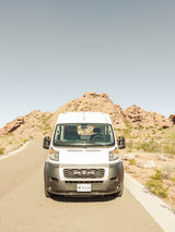 White RV rental van parked on a desert road amidst red rock formations under a clear sky.