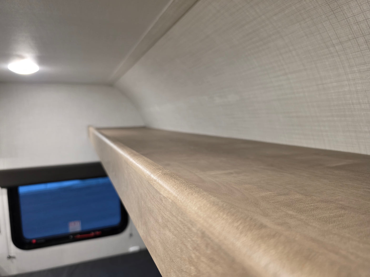 Inside an RV rental, a sturdy bunk bed provides extra sleeping space. View of window below and ceiling light.