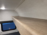 Inside an RV rental, a sturdy bunk bed provides extra sleeping space. View of window below and ceiling light.