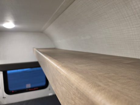 Inside an RV rental, a sturdy bunk bed provides extra sleeping space. View of window below and ceiling light.