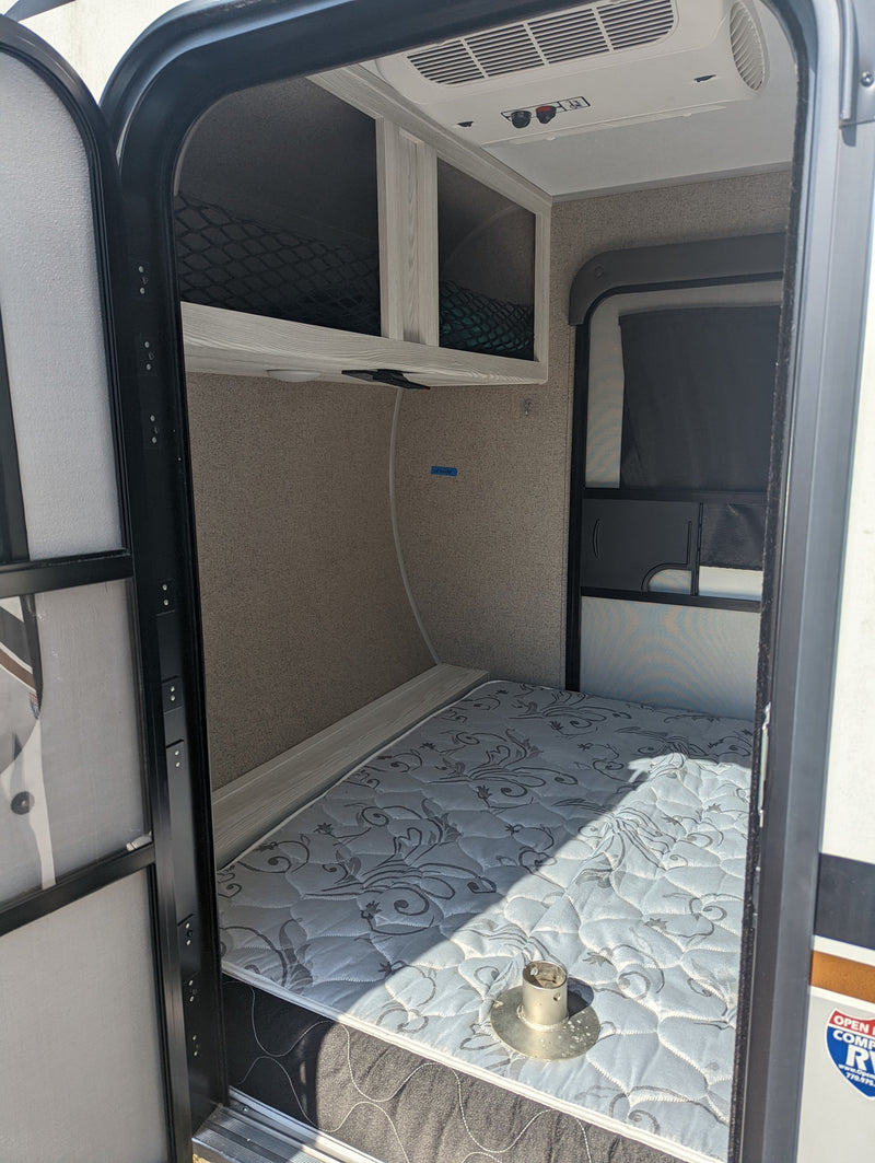Step into this RV rental, featuring a lower bunk bed with mattress, upper storage cubbies, and overhead AC unit. — photo 12