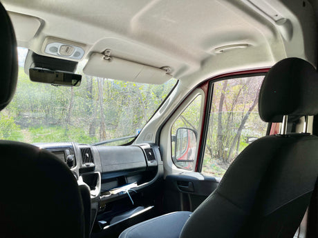 View from inside an RV rental, showing the dashboard, seats, and a natural, green landscape through the windshield.