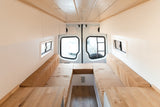 Step inside this bright RV rental! Modern camper van interior with light wood & white finishes, featuring convertible bench seating.