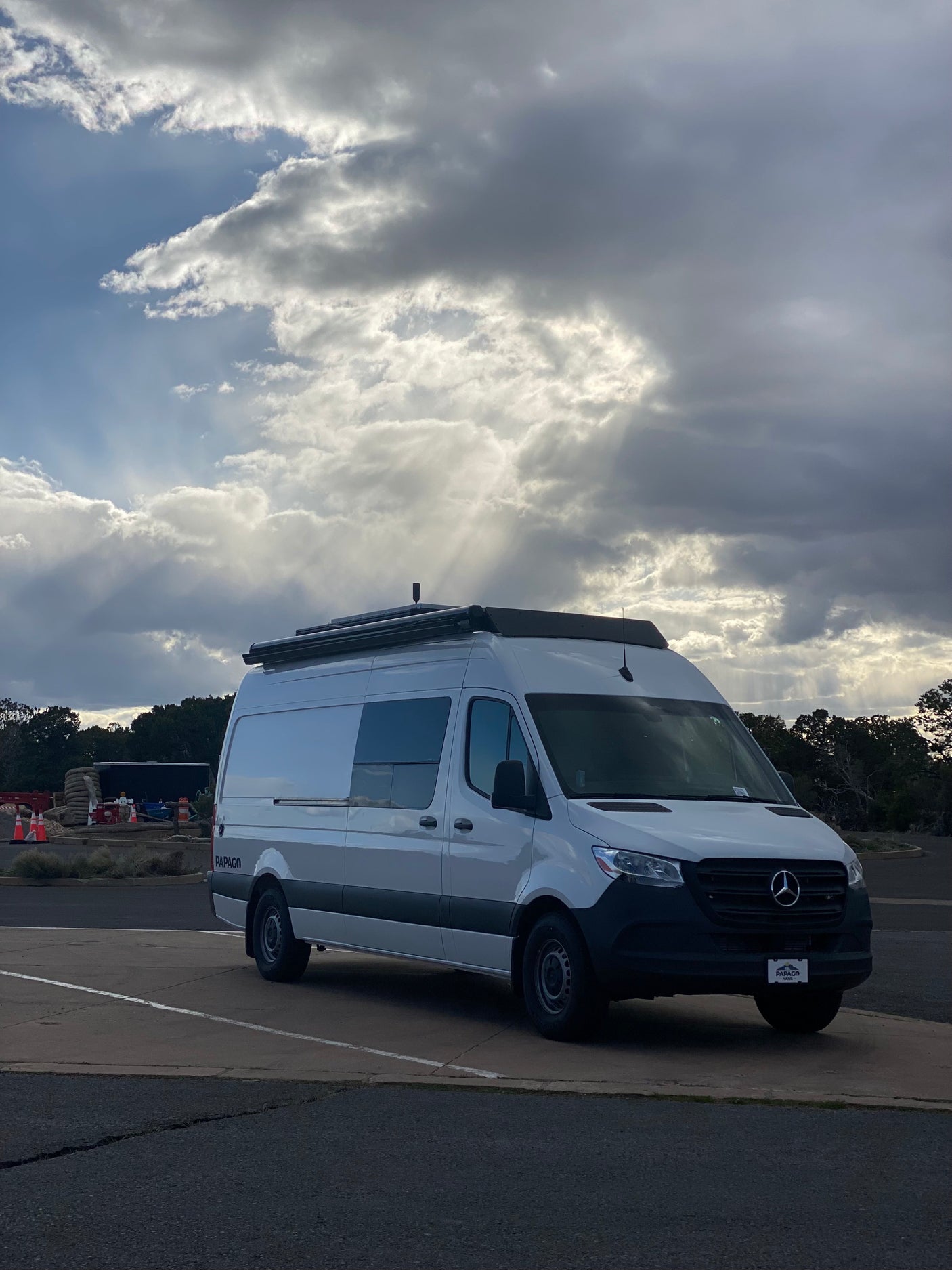 A white Mercedes-Benz Sprinter RV rental parked under a dramatic sky with sun rays. Ideal for scenic travel and adventure.