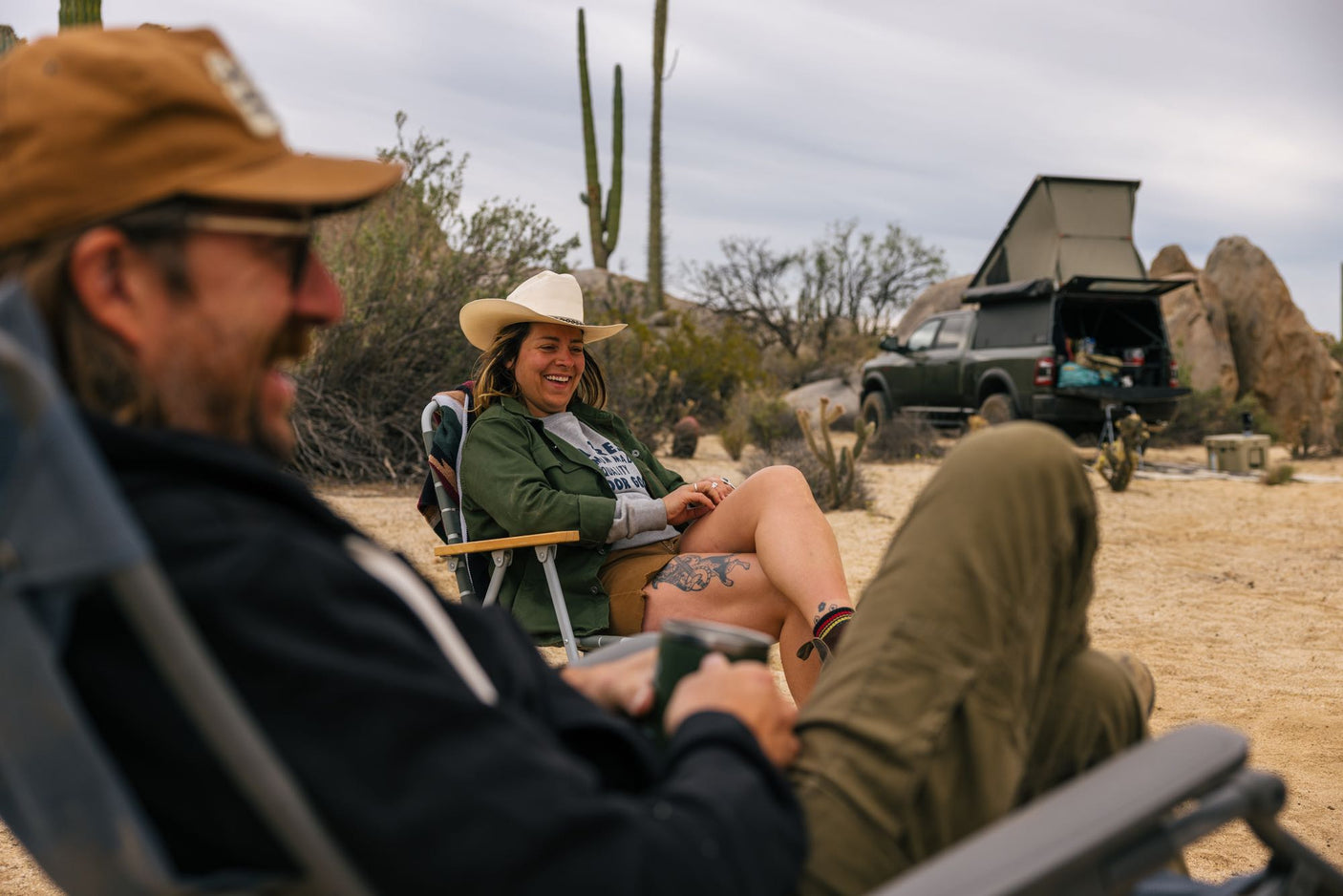 Desert camping: A laughing woman in a cowboy hat relaxes by her RV rental truck with an overlanding tent.
