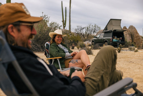 Desert camping: A laughing woman in a cowboy hat relaxes by her RV rental truck with an overlanding tent.