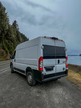 Light gray camper van, an RV rental, parked on a scenic coastal road. Perfect for nature exploration under cloudy skies.