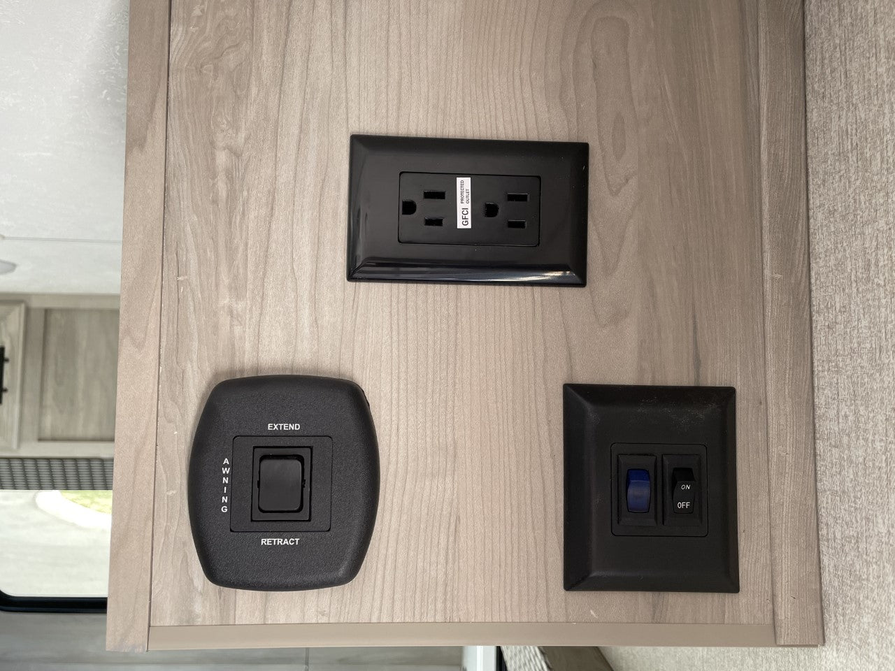 RV rental interior wall with black GFCI power outlet, awning control, and two ON/OFF switches. Essential RV amenities.