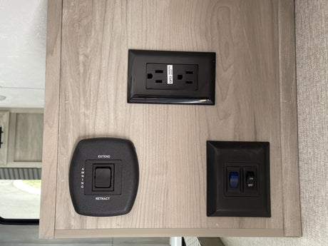 RV rental interior wall with black GFCI power outlet, awning control, and two ON/OFF switches. Essential RV amenities.