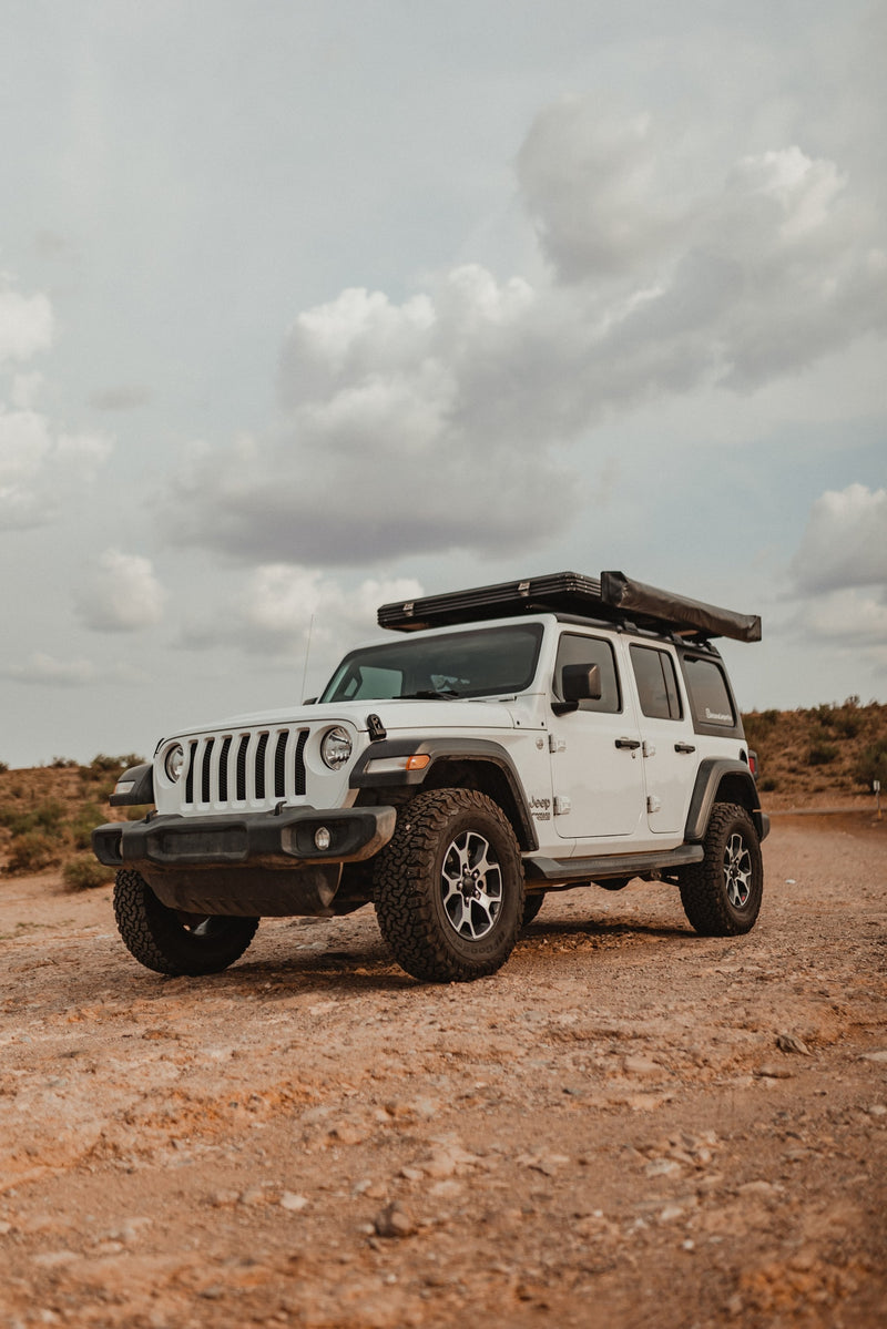 White Jeep Wrangler RV rental with rooftop tent & awning on a dirt road under a cloudy sky, ready for adventure. — photo 9