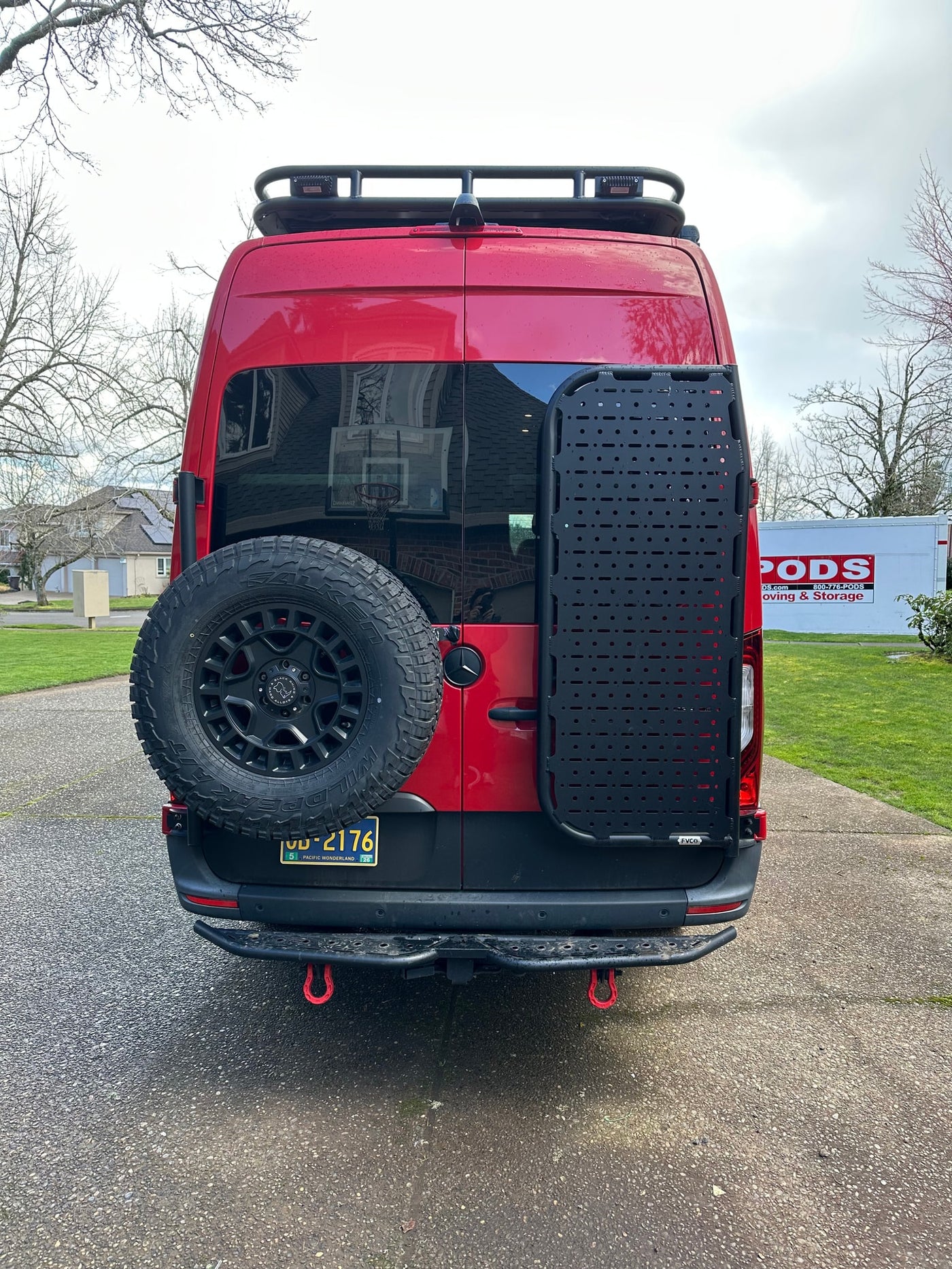 Rear view of a red custom camper van, equipped for travel with a spare tire, gear panel, and roof rack. Perfect for an RV rental adventure. — photo 3