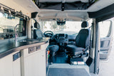 Inside an RV rental: a modern camper van interior featuring a kitchen with sink, cozy living space, and driver's cabin.