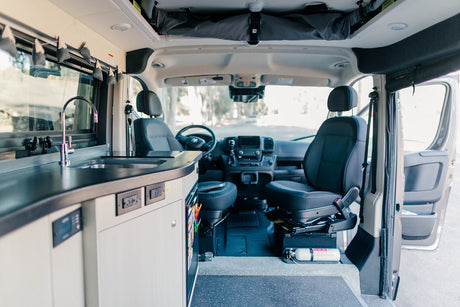 Inside an RV rental: a modern camper van interior featuring a kitchen with sink, cozy living space, and driver's cabin.