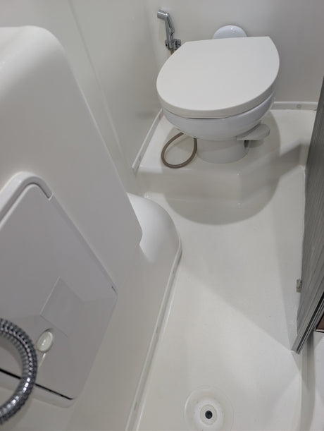 RV rental: Compact, all-white bathroom with a toilet, bidet sprayer, shower hose, and floor drain, optimizing space for travel.