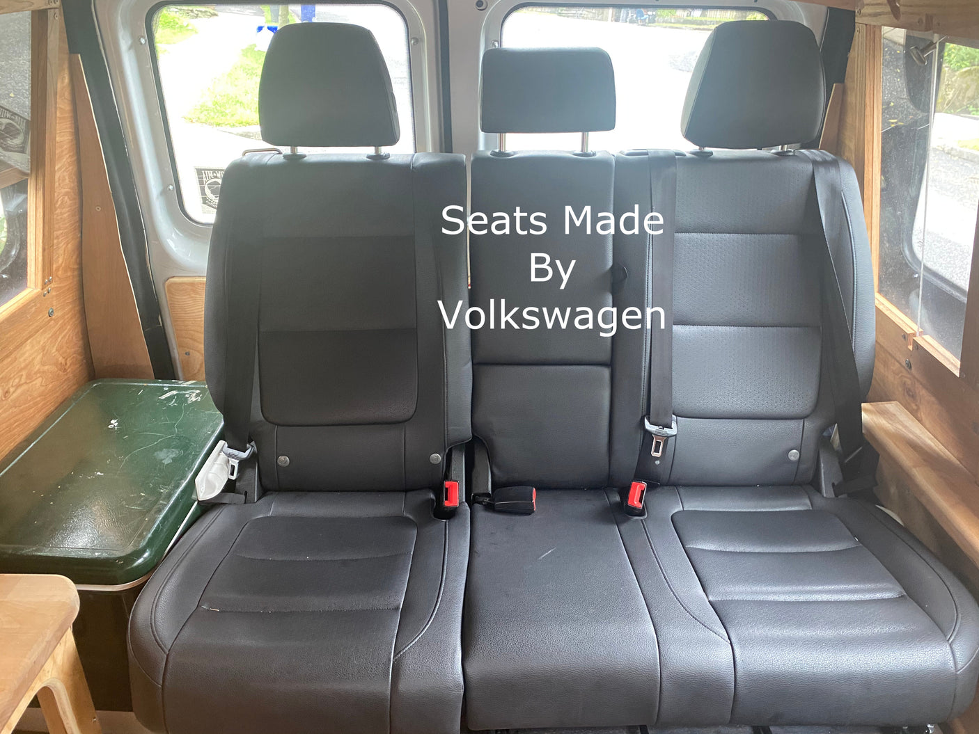 RV rental: Three black Volkswagen seats with seatbelts, inside a custom van interior with wood trim and cooler.