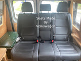 RV rental: Three black Volkswagen seats with seatbelts, inside a custom van interior with wood trim and cooler.