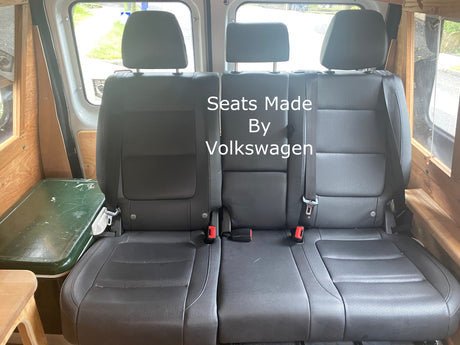 RV rental: Three black Volkswagen seats with seatbelts, inside a custom van interior with wood trim and cooler.