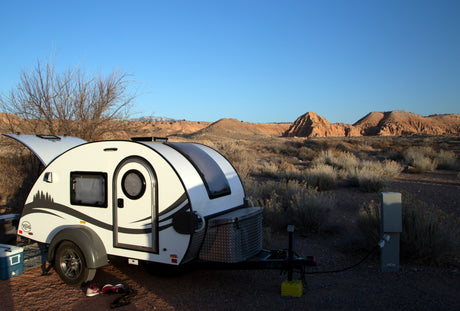 White teardrop **rv rental** at a desert campsite, powered up for a tranquil getaway amidst rugged mountains.