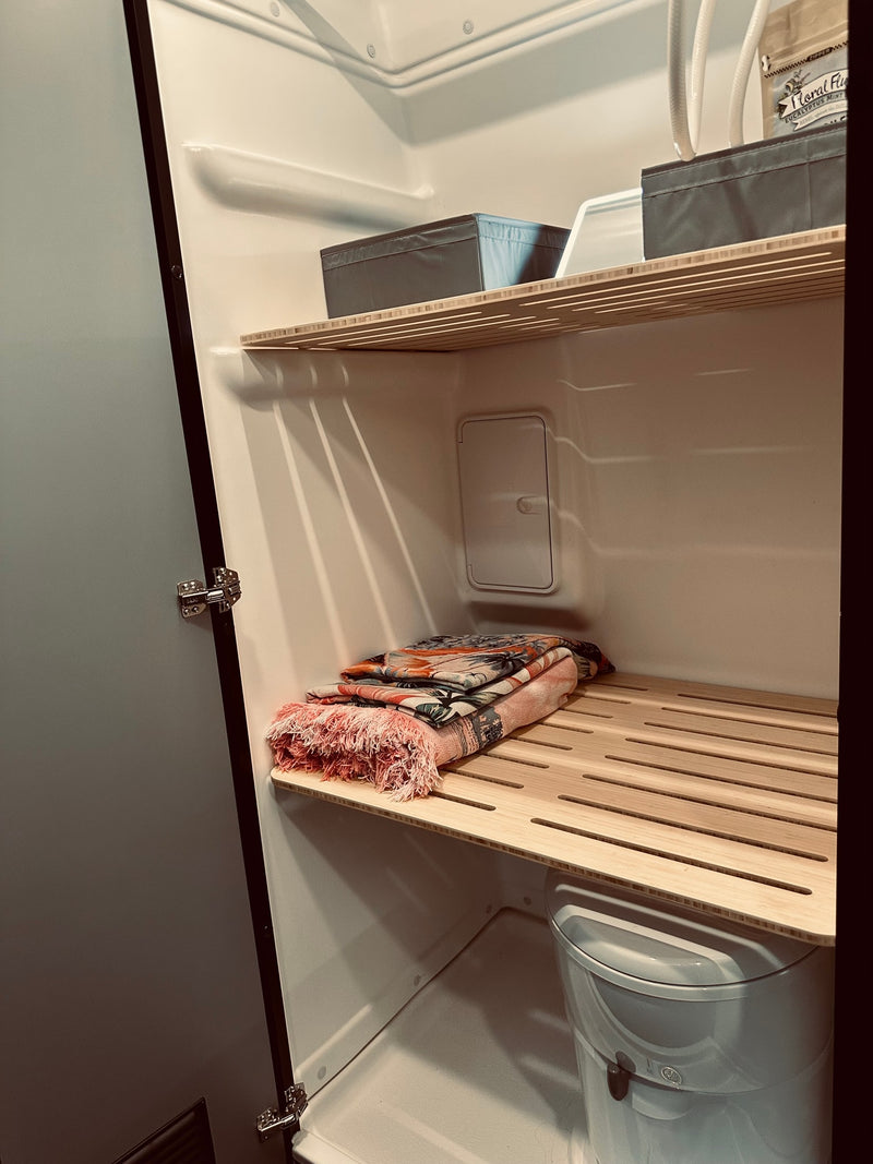 Inside an RV rental's compact bathroom, showing slatted wooden shelves with storage bins, folded blankets, and a toilet. — photo 7