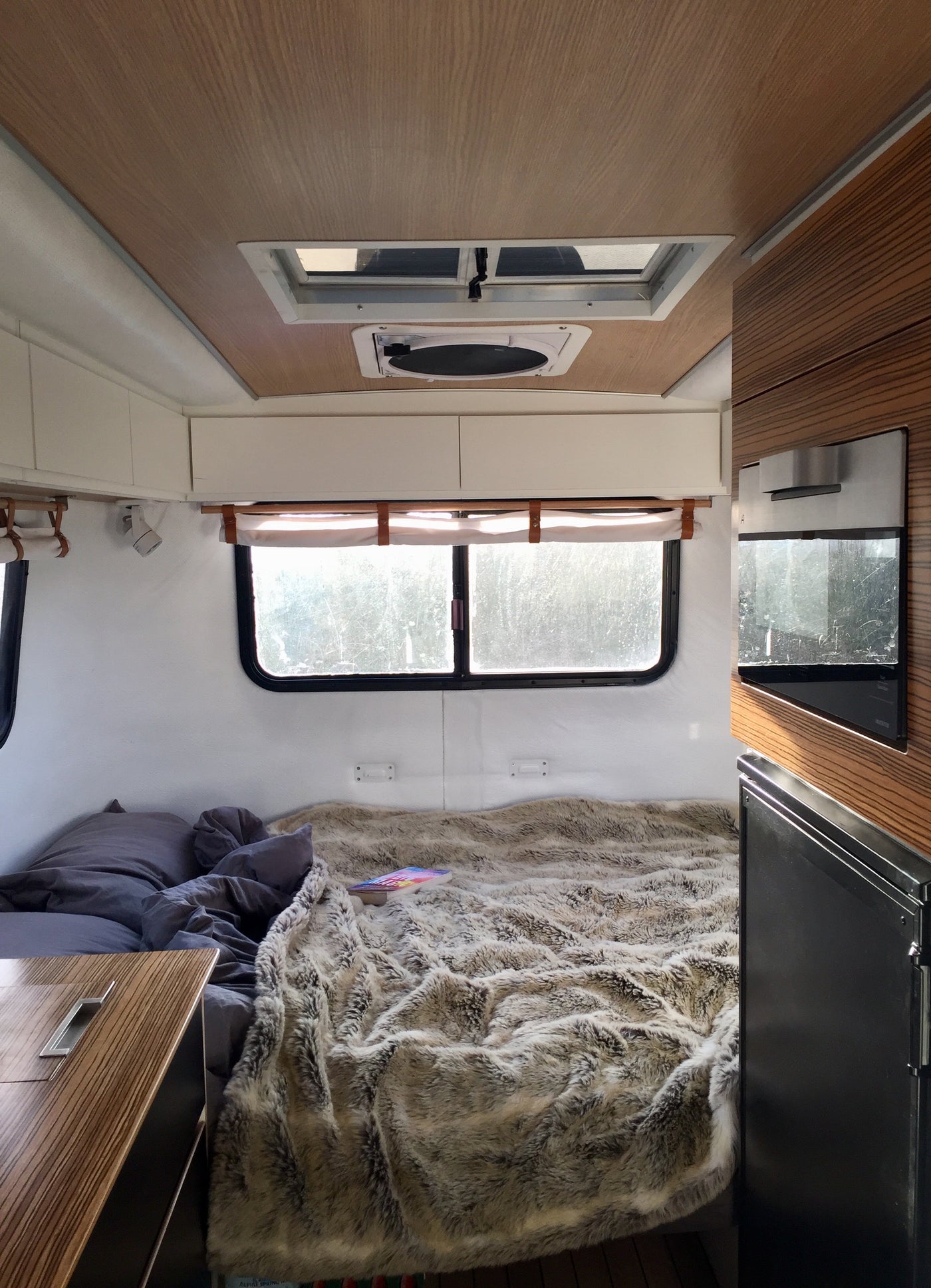 Cozy RV rental interior: Bedroom with plush blanket, bright windows, and compact kitchenette for your next adventure. — photo 14