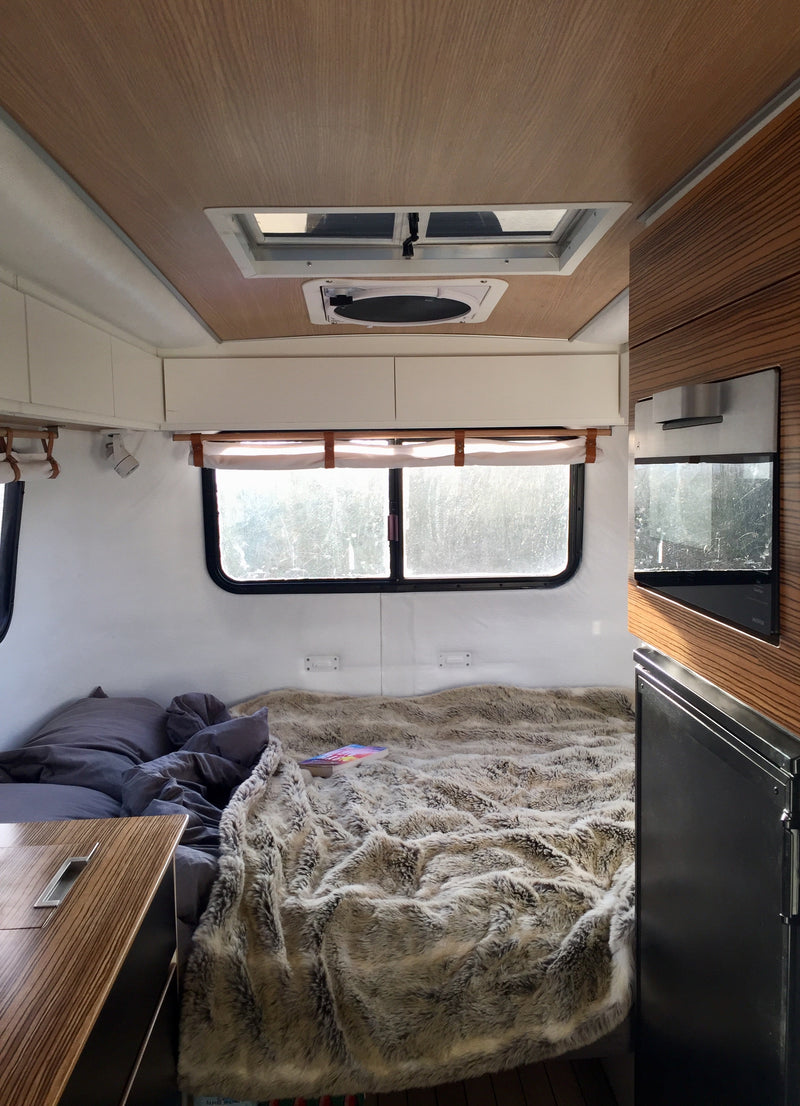 Cozy RV rental interior: Bedroom with plush blanket, bright windows, and compact kitchenette for your next adventure. — photo 14