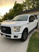 White Ford F-150 pickup with bed rack on driveway. Perfect for adventures, an RV rental alternative.