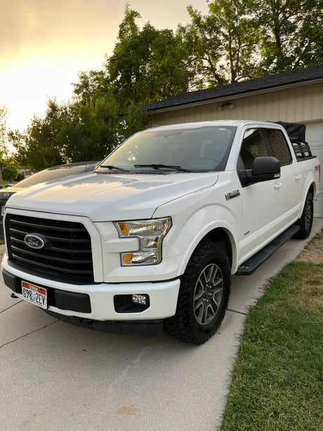 White Ford F-150 pickup with bed rack on driveway. Perfect for adventures, an RV rental alternative.