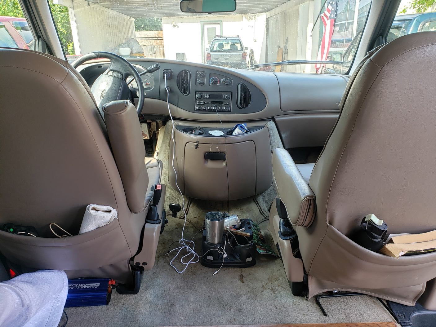 Inside an RV rental Ford van: dashboard, front seats, and floor with a power inverter & supplies for travel.